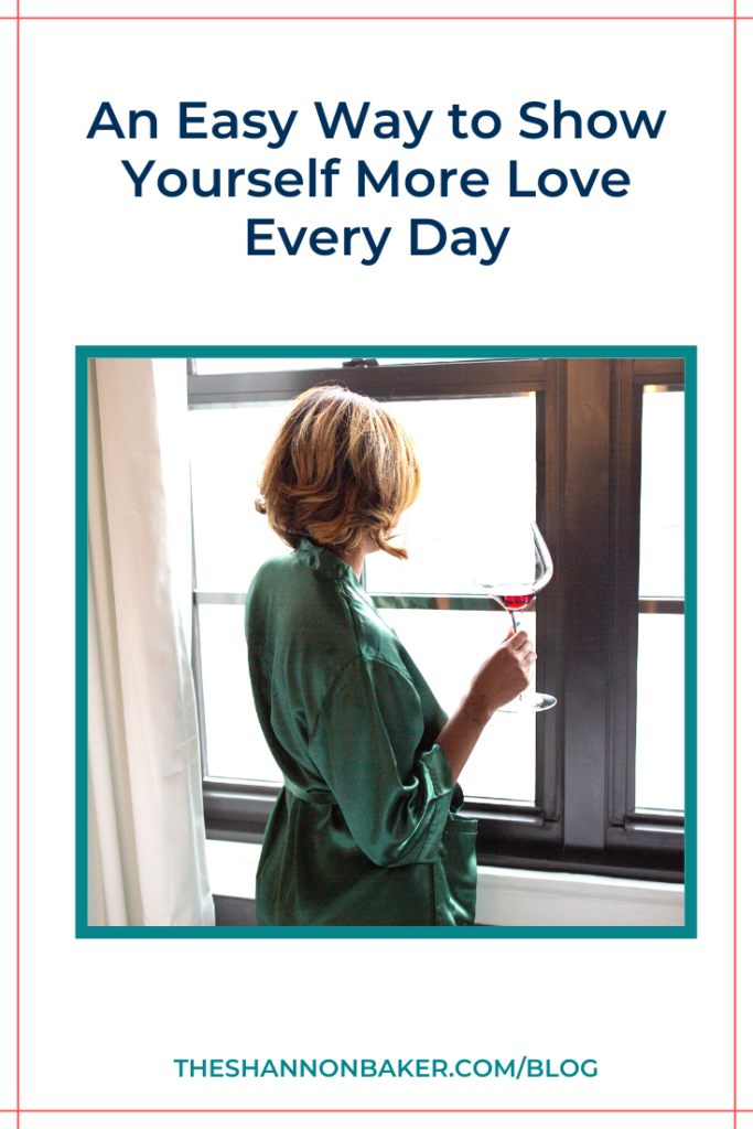 The words "An Easy Way to Show Yourself More Love Every Day" above the image of a woman wearing a green silk robe looking out the windows with a glass of red wine in her right hand