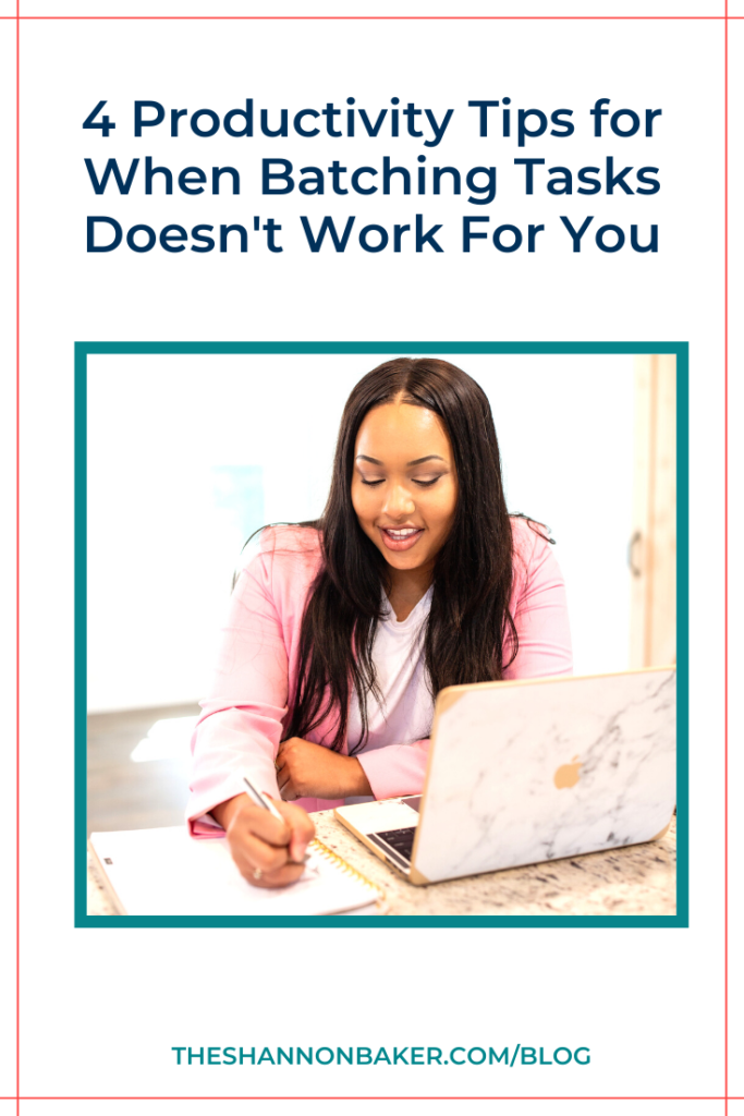 The words "4 Productivity Tips for When Batching Tasks Doesn't Work For You" on plain white background above square image of a woman wearing a pink jacket and a white shirt. She is sitting at the desk with her Macbook open in front of her and is smiling looking down and writing on a notepad.